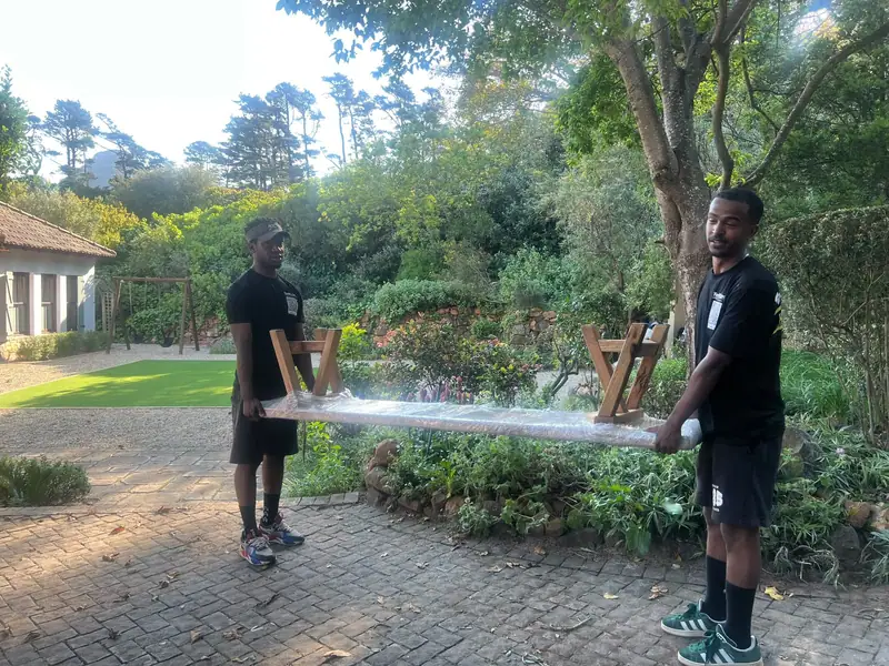 Two team members carrying a wrapped wooden bench through a customer's garden